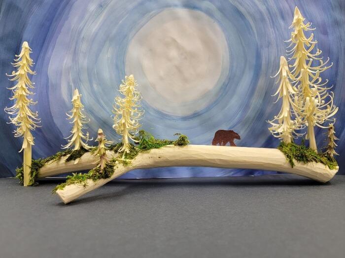 Bear walking across log surrounded by whittled trees, moon and dark blue sky in the background